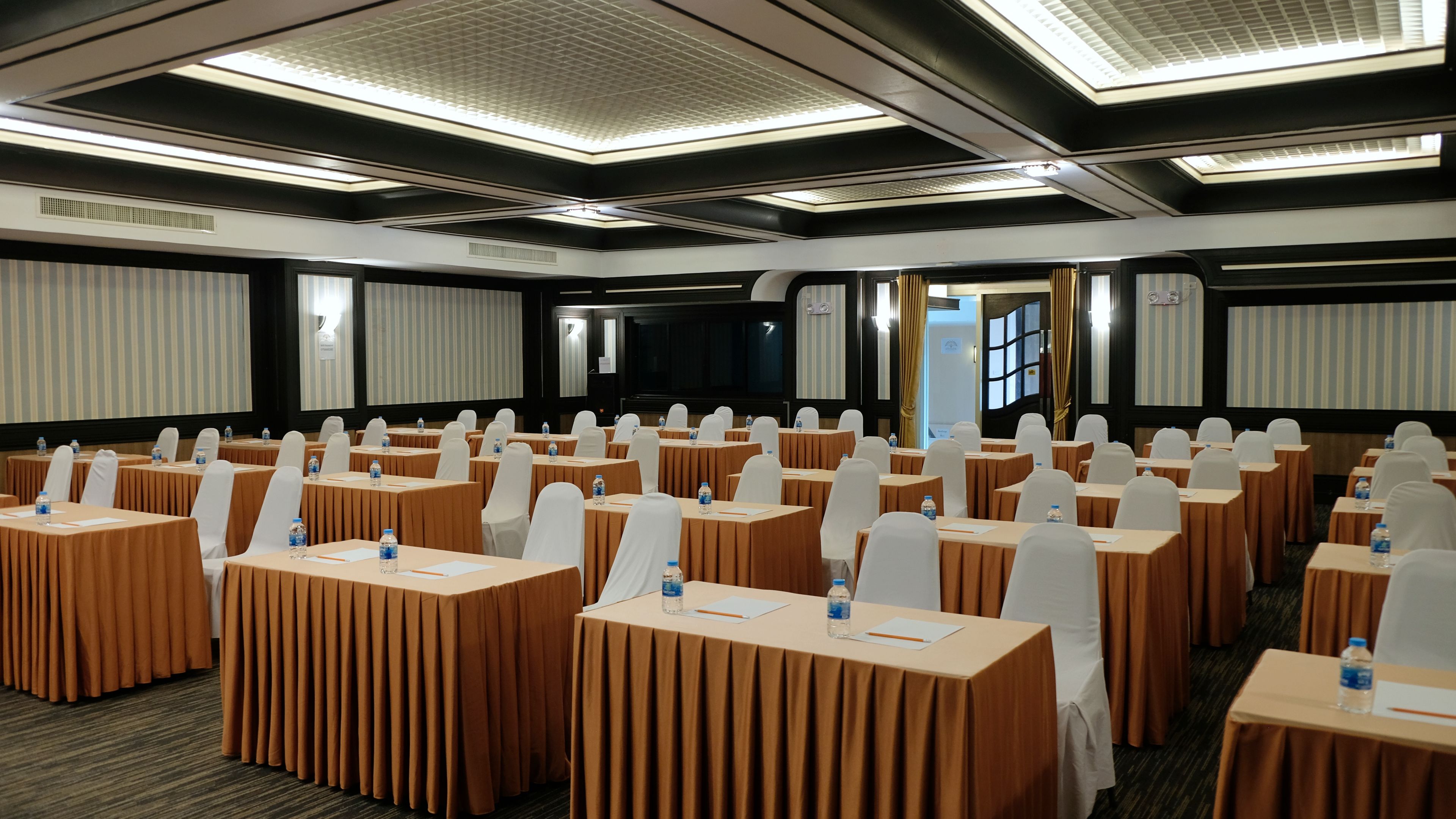 A conference room with rows of tables, chairs, and a large screen.