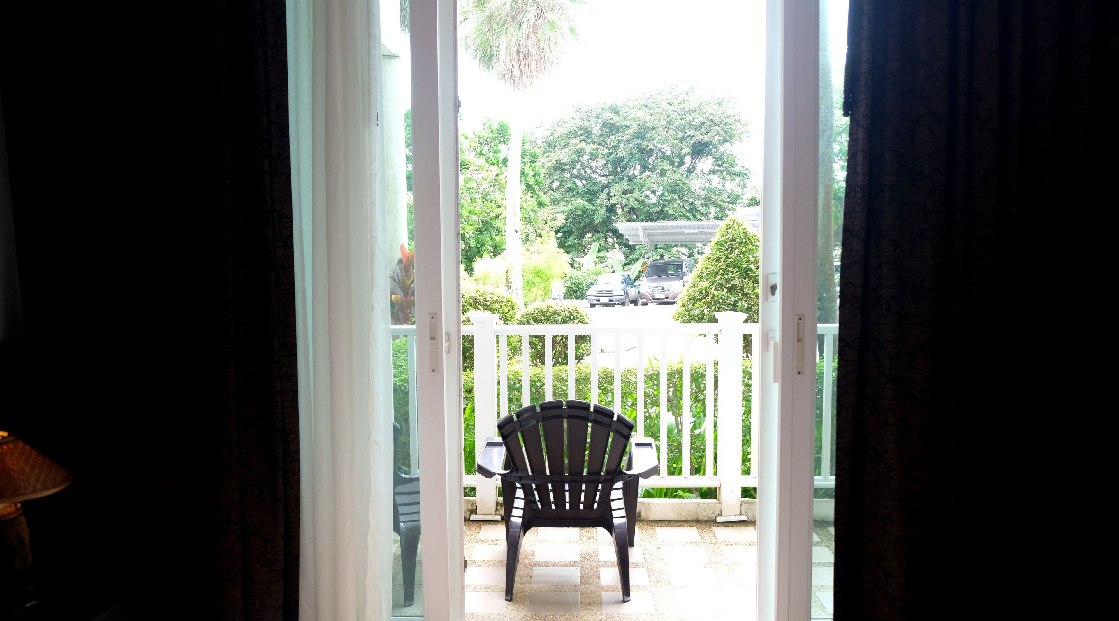 A view through a doorway to an outdoor area with a white fence, a black plastic chair, and a table.