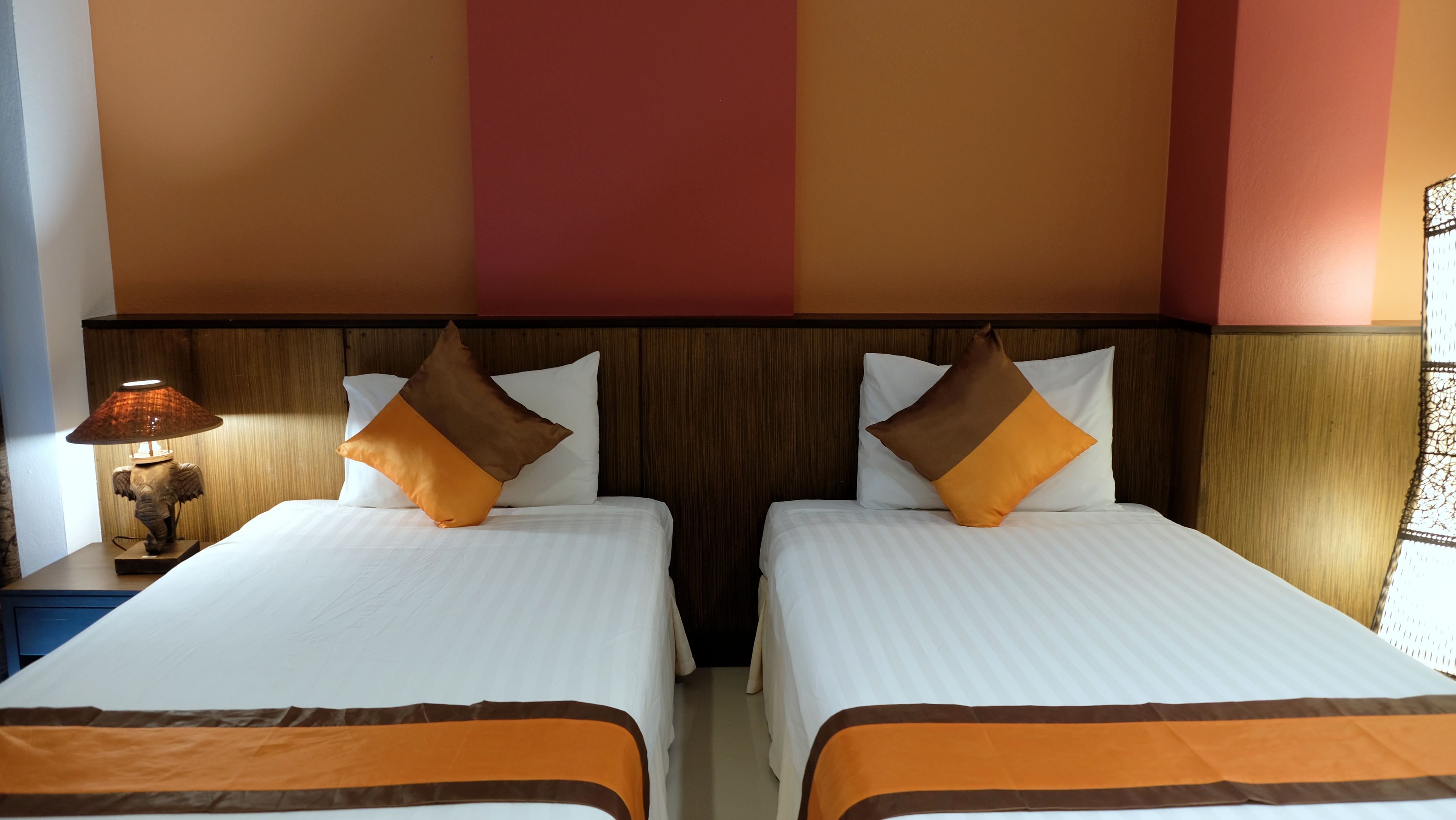 A hotel room with two beds, a nightstand with a lamp, and a wooden headboard.