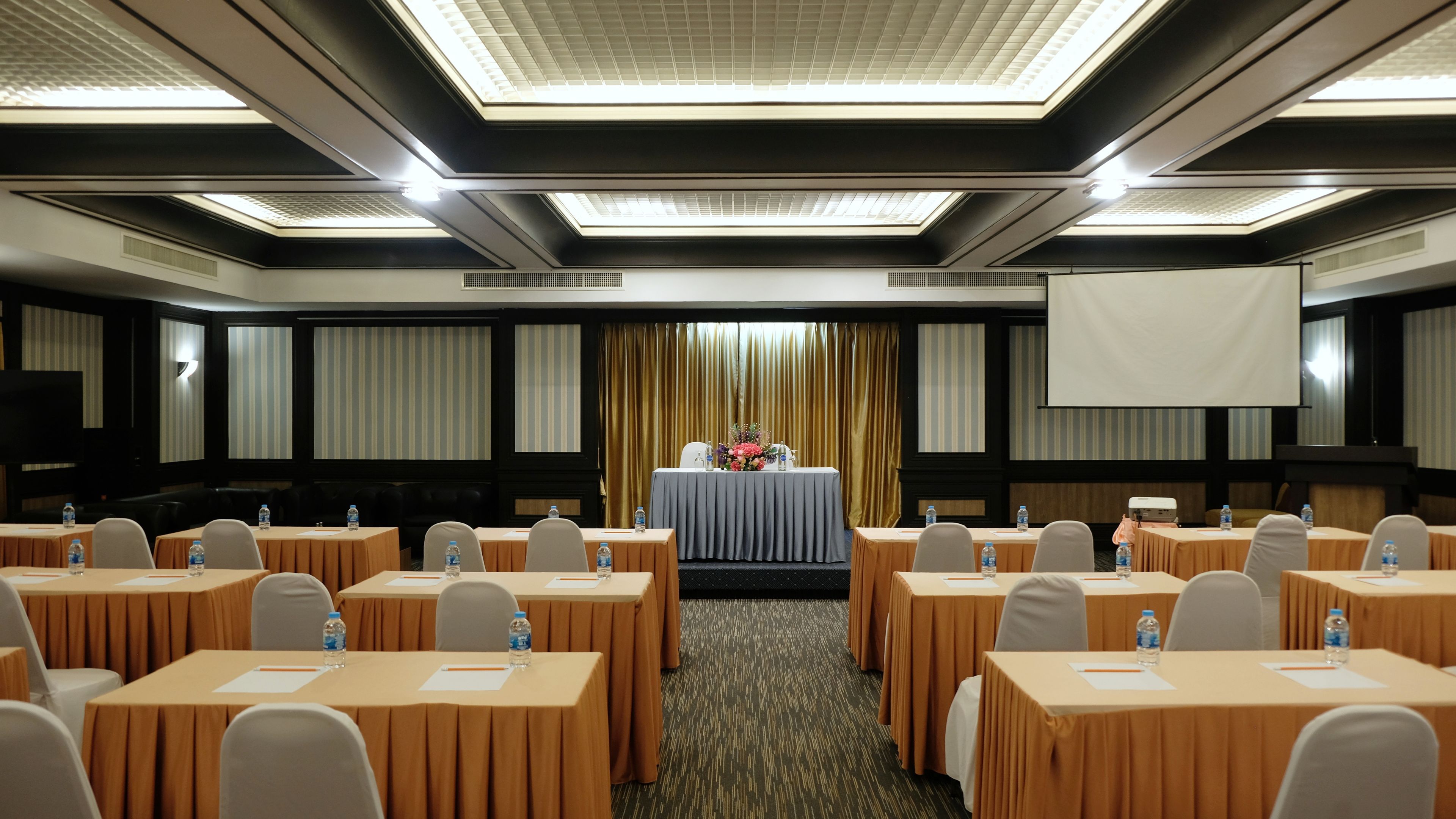 A conference room with tables, chairs, a projector screen, and a floral arrangement.