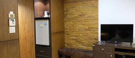 A compact kitchen with a refrigerator, a coffee maker, and a wooden bench.