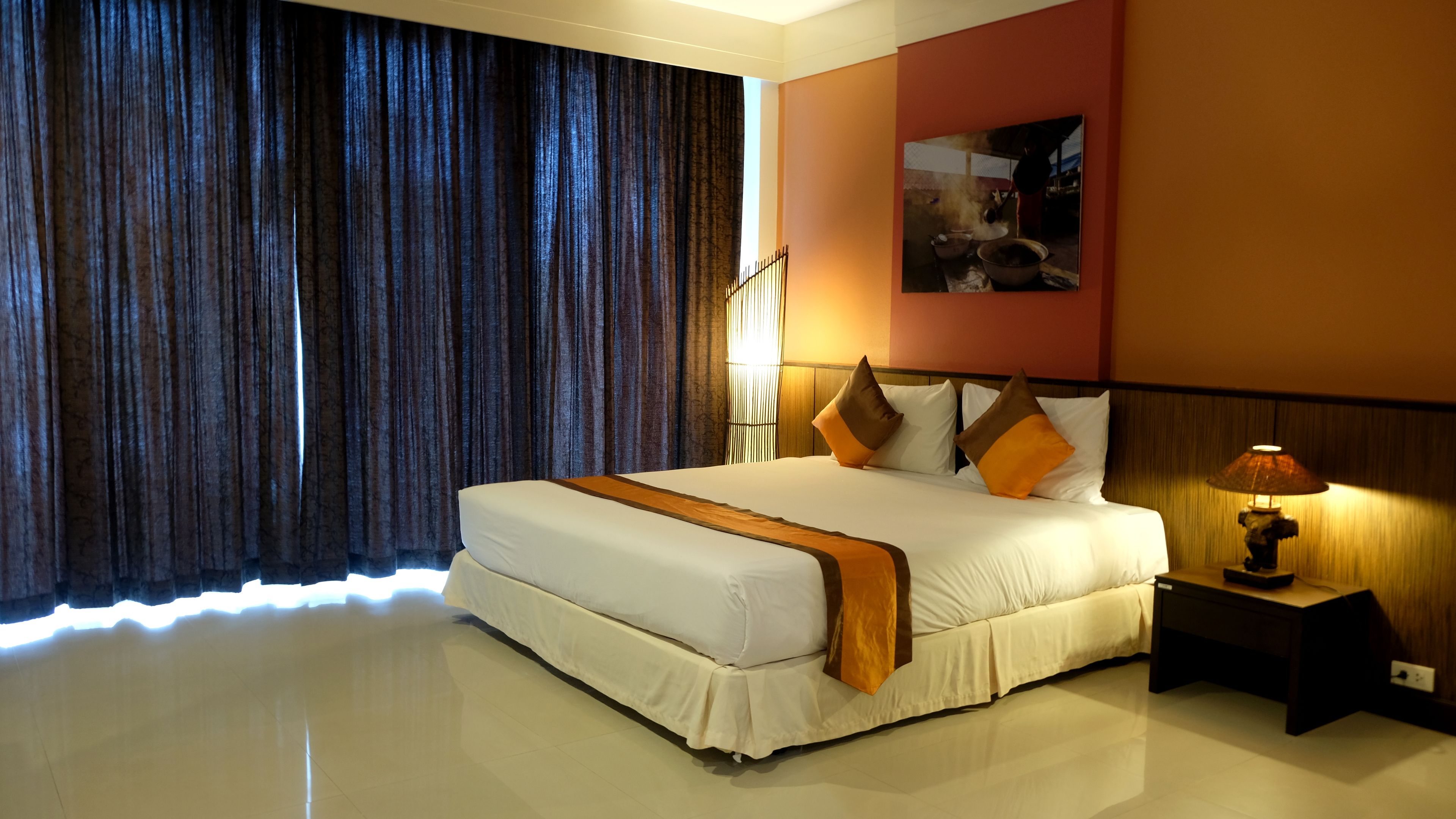 A hotel room with a large bed, a nightstand with a lamp, and a painting on the wall.