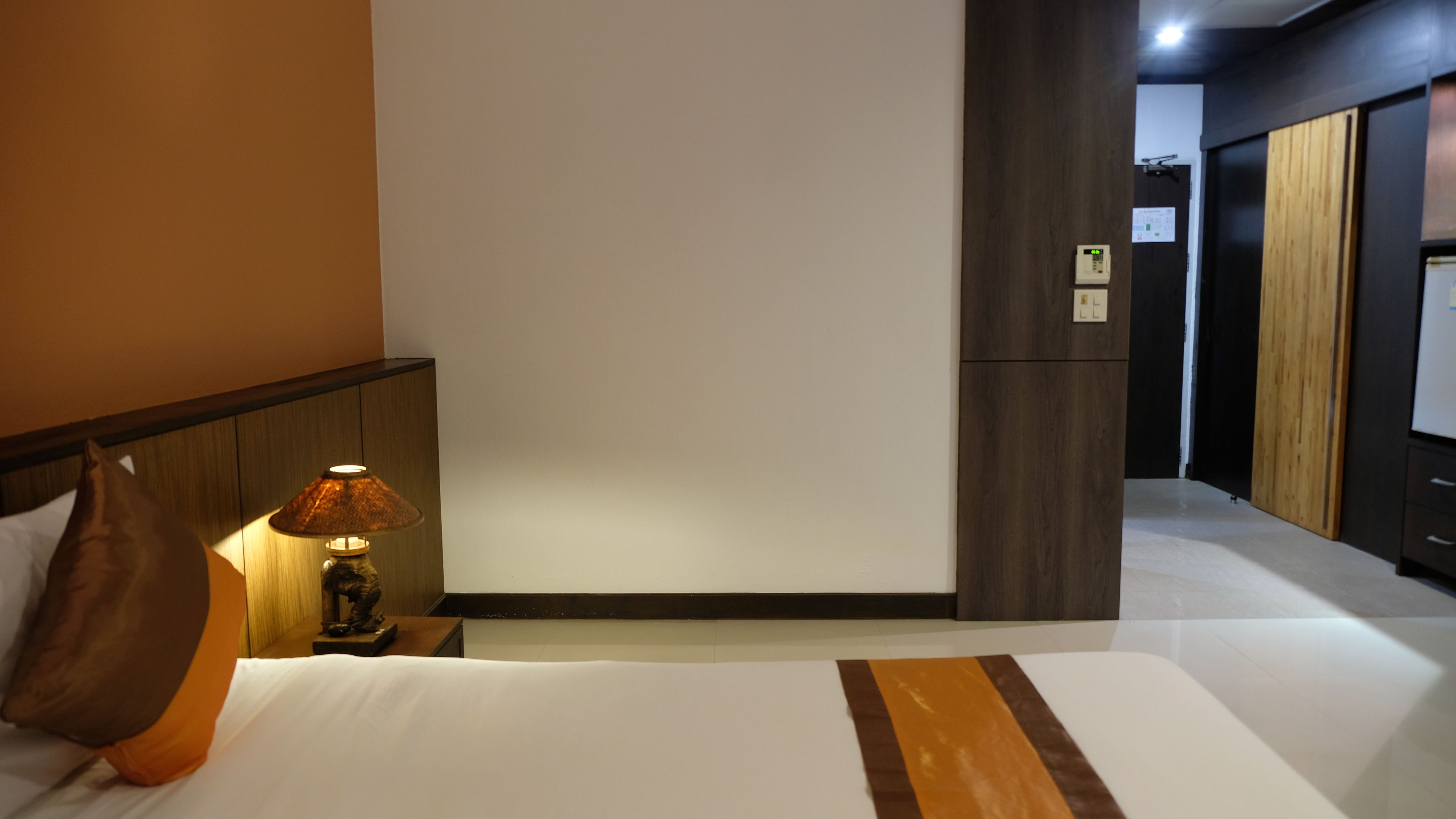 A hotel room with a bed, a nightstand with a lamp, a wooden headboard, and a wardrobe.