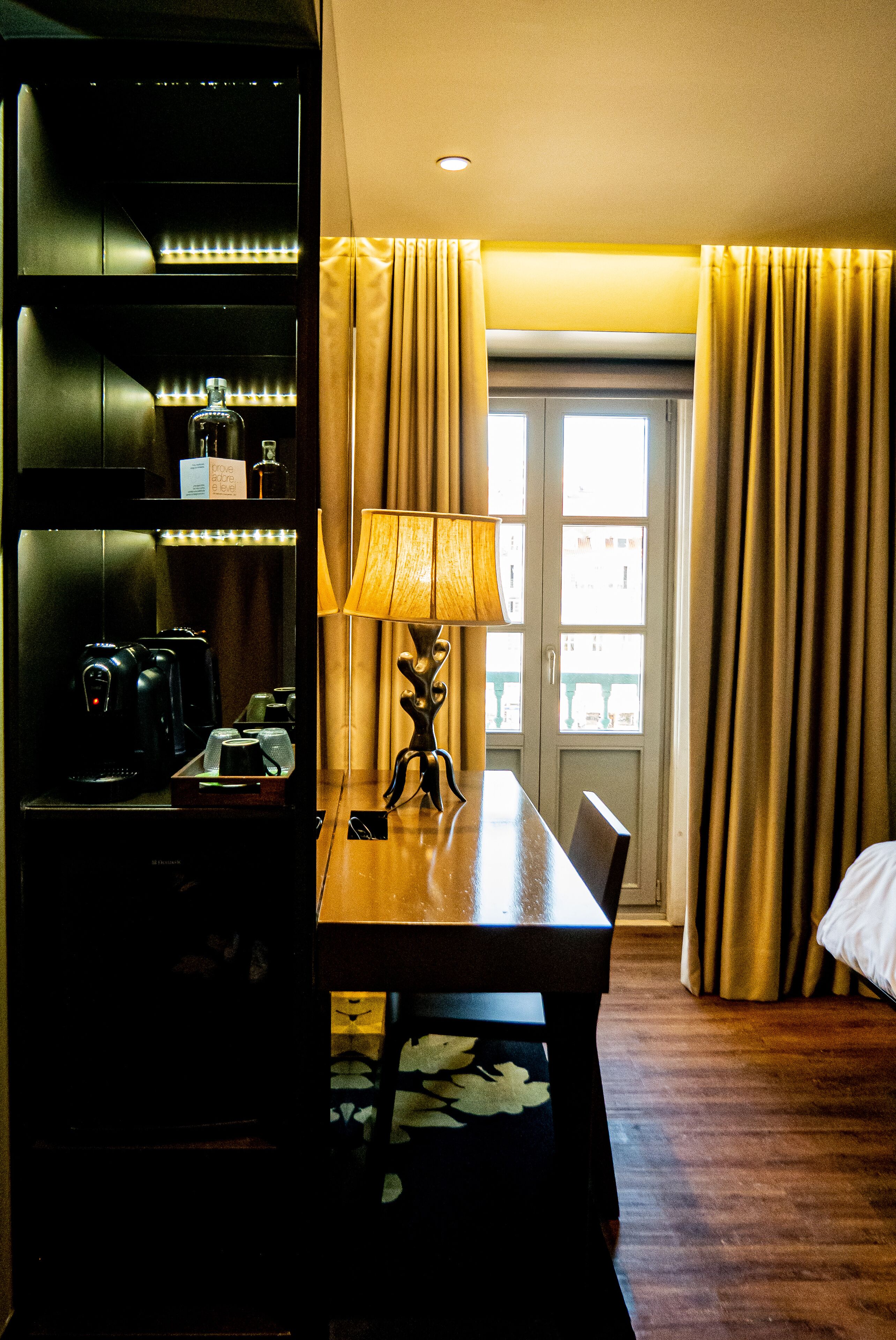 Une chambre d’hôtel avec une table en bois, une lampe, une machine à café et un mini-bar.