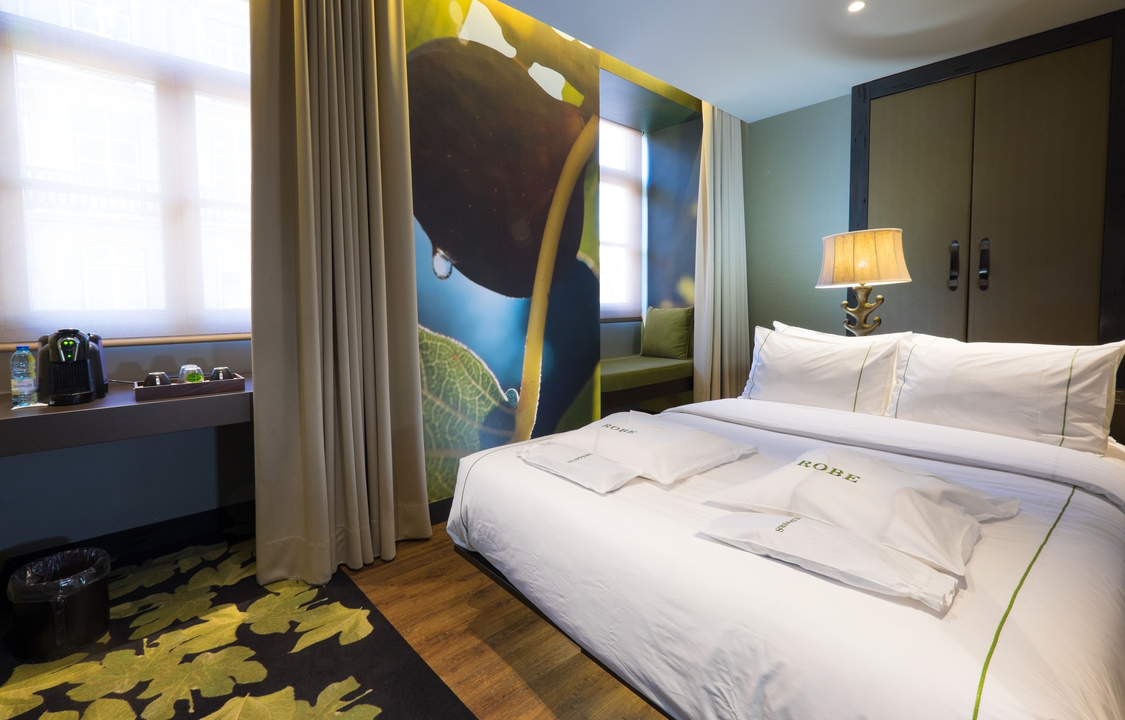 A hotel room with a bed, a desk, a lamp, and a wardrobe.