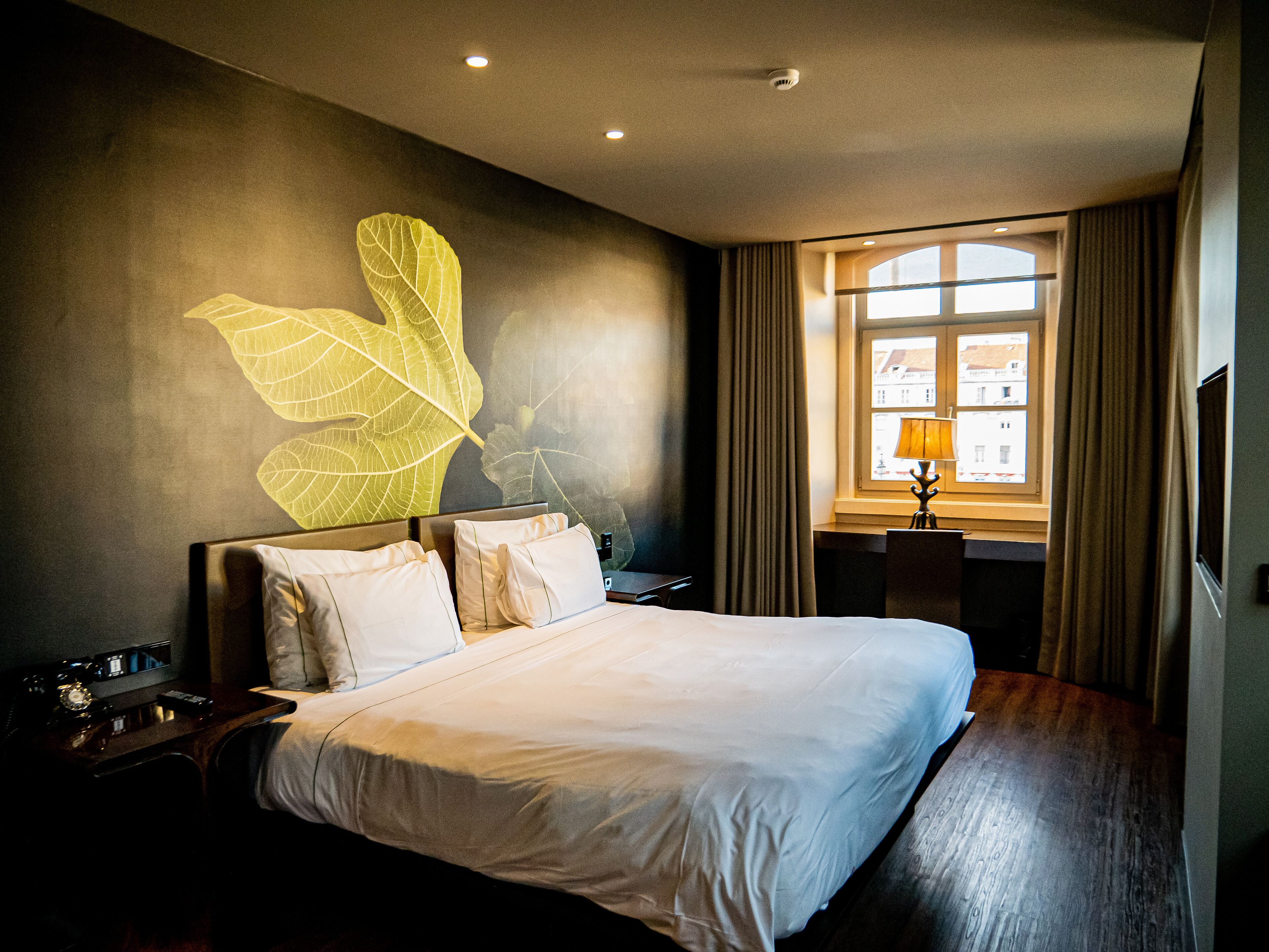 Une chambre d’hôtel avec un grand lit, un bureau avec une lampe et une fenêtre avec des rideaux.