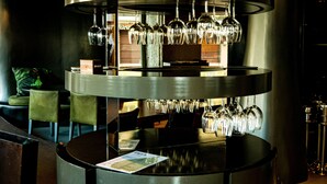 A circular bar area with multiple levels of wine glasses and bottles, surrounded by green chairs and a wooden counter. - Figueira by The Beautique Hotels & SPA (Lisbon)