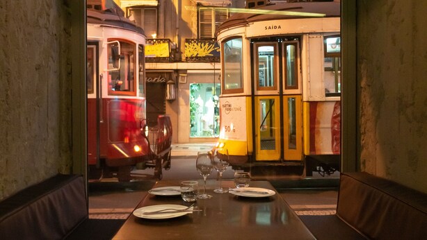 A dining area with a table set for two, a bench, and a view of vintage trams passing by. - Figueira by The Beautique Hotels & SPA (Lisbon)