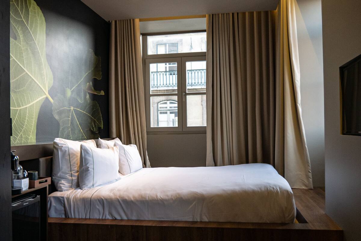 Une chambre d’hôtel moderne avec un grand lit, un plancher en bois, une fenêtre avec des rideaux et un téléviseur fixé au mur.