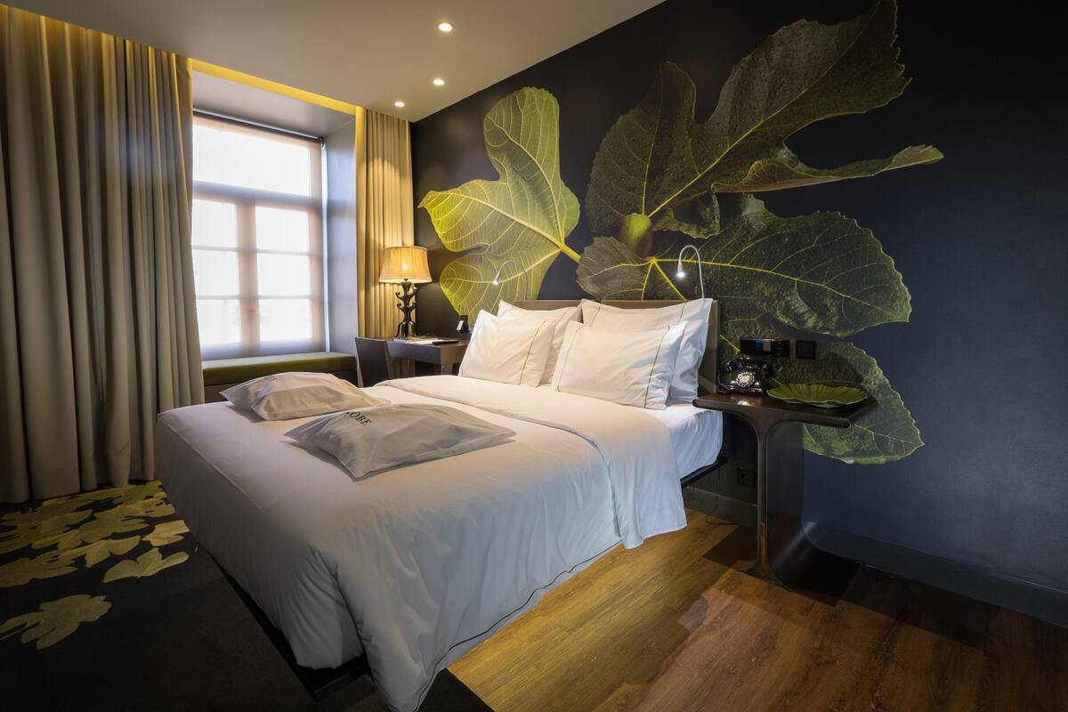 Une chambre d’hôtel avec un grand lit, une table de chevet avec une lampe et une grande fresque murale représentant des feuilles.
