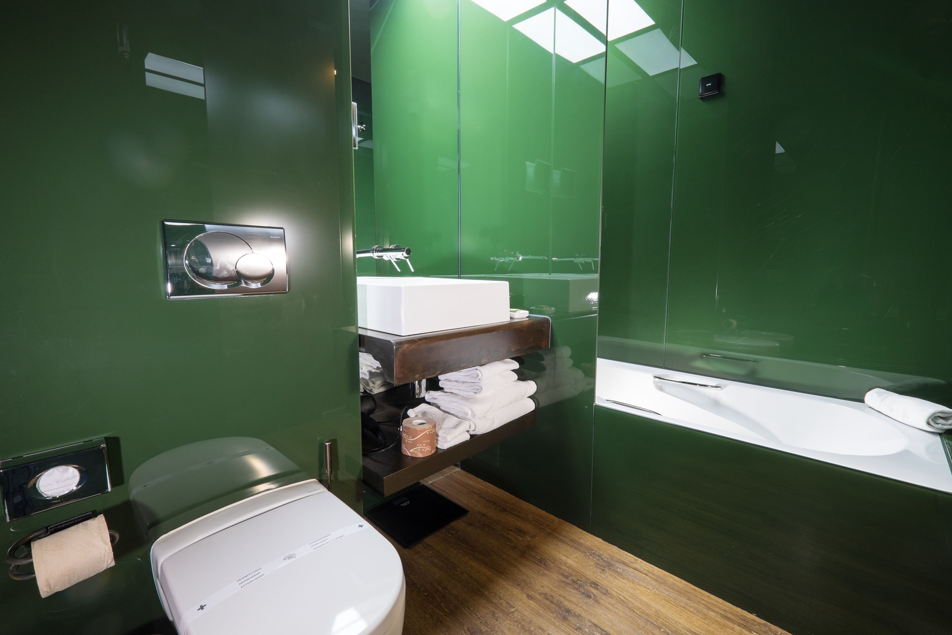 A modern bathroom with a green wall, a white sink, a mirror, and a wooden floor.
