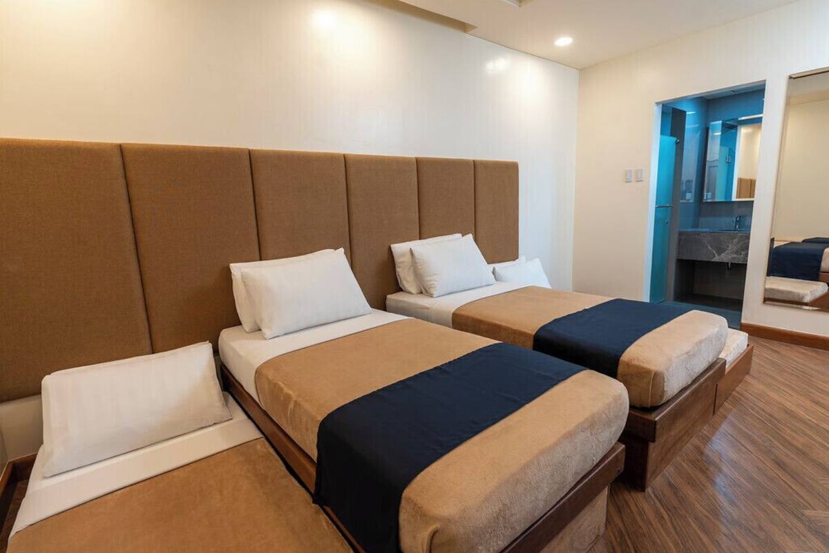 A hotel room with two beds, a large headboard, a bathroom with a mirror, and a wooden floor.