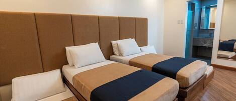 Habitación de hotel con dos camas, un cabecero grande, un baño con espejo y suelo de madera.