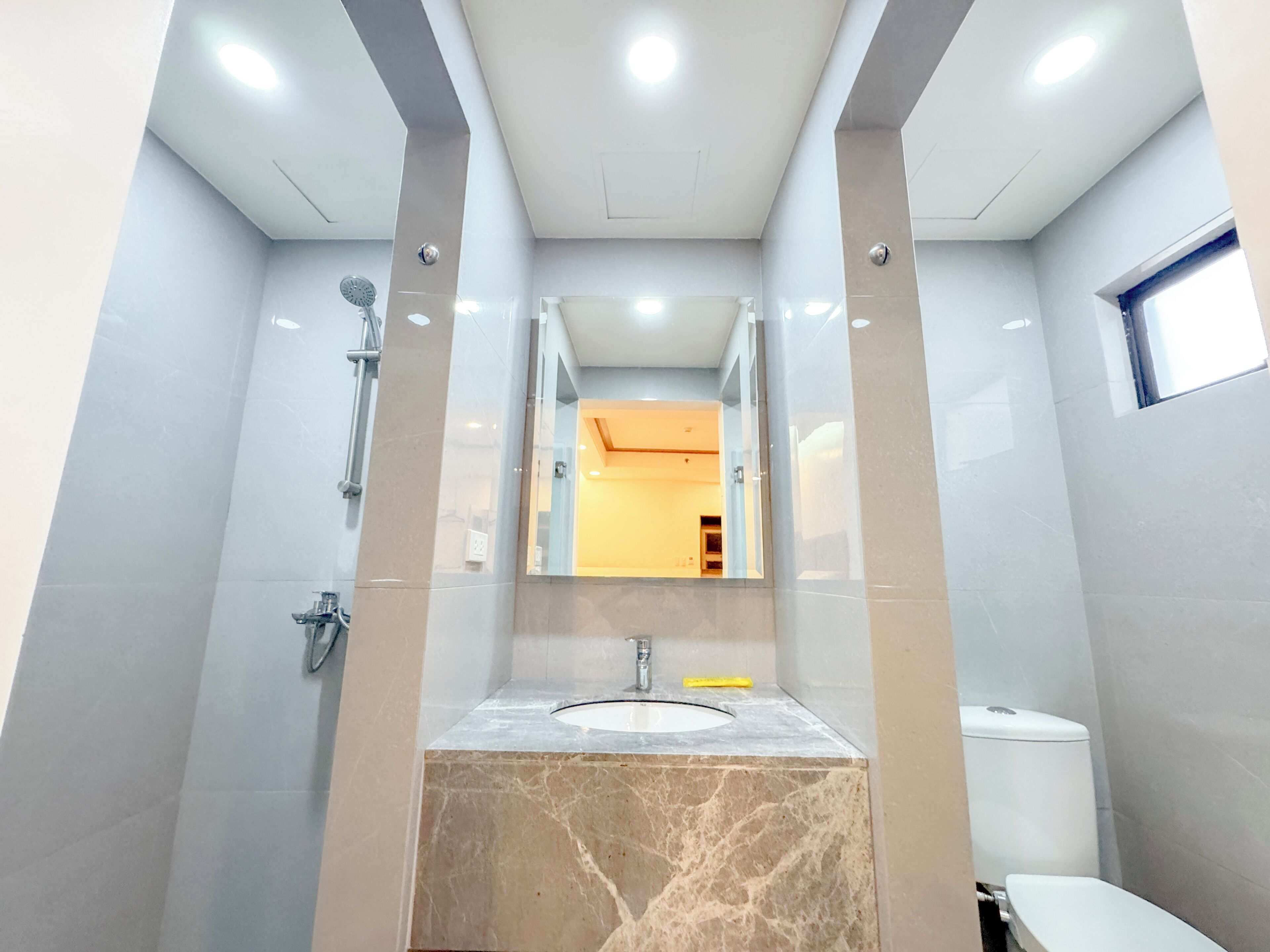 A modern bathroom with a marble sink, a mirror, a shower, and a toilet.