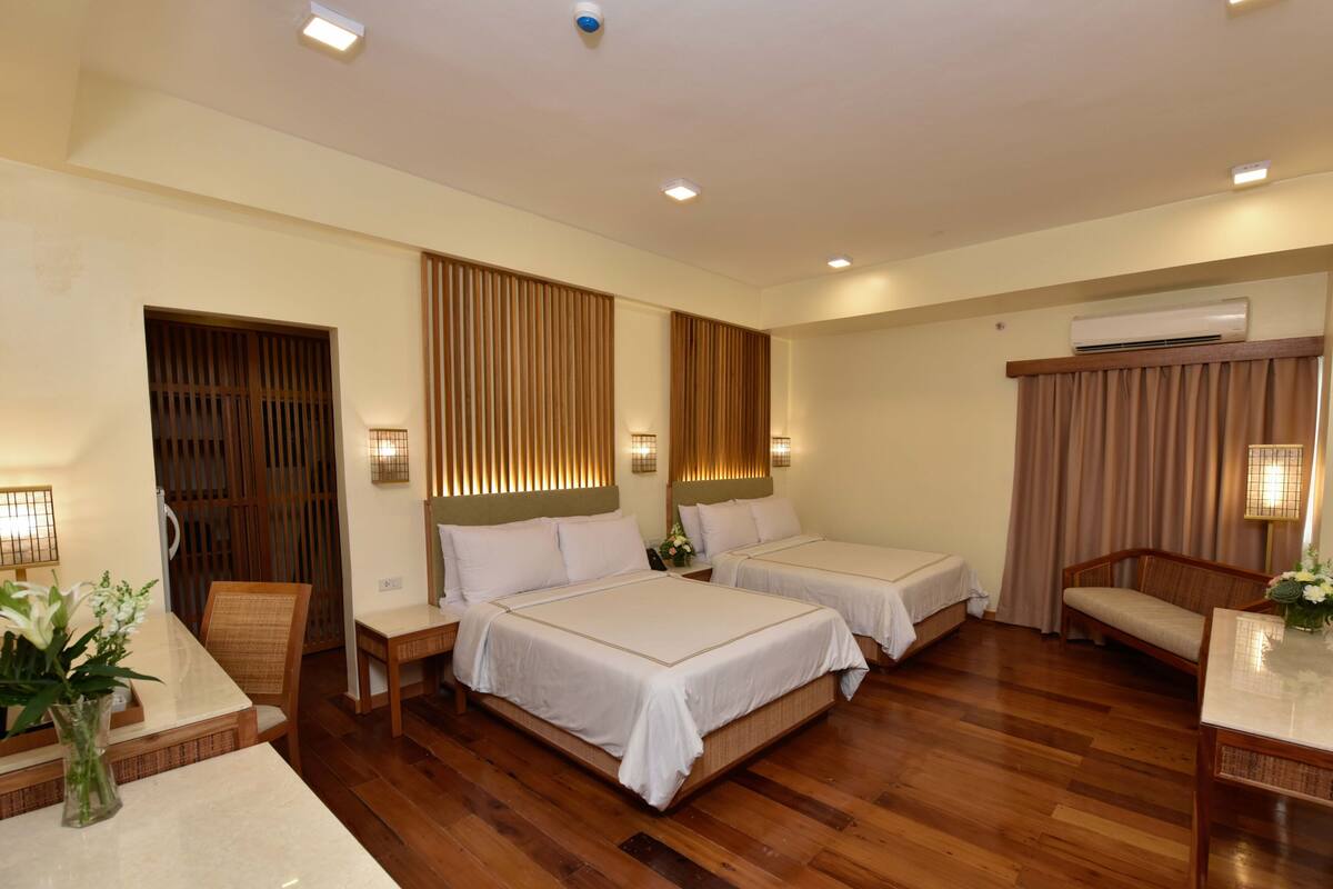 A hotel room with two beds, a desk, a chair, and a TV.
