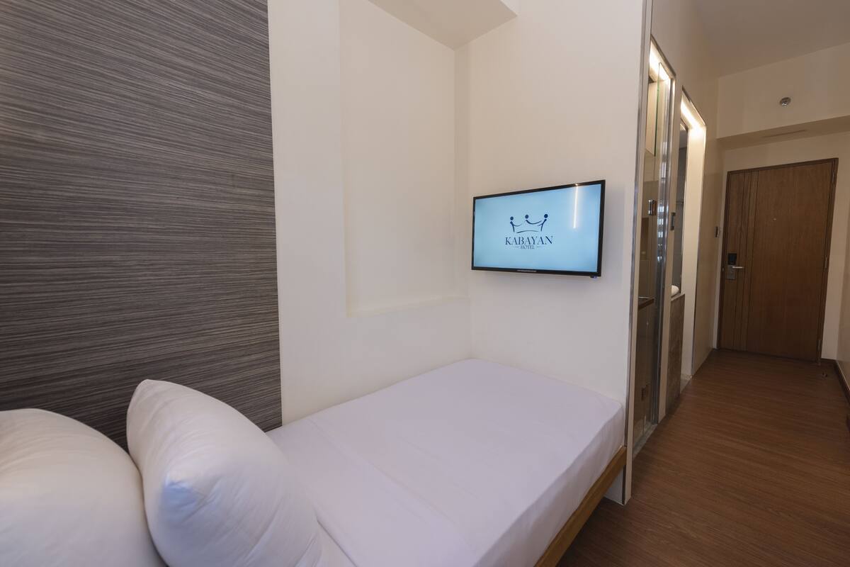 A hotel room with a bed, a TV mounted on the wall, and a wooden floor.