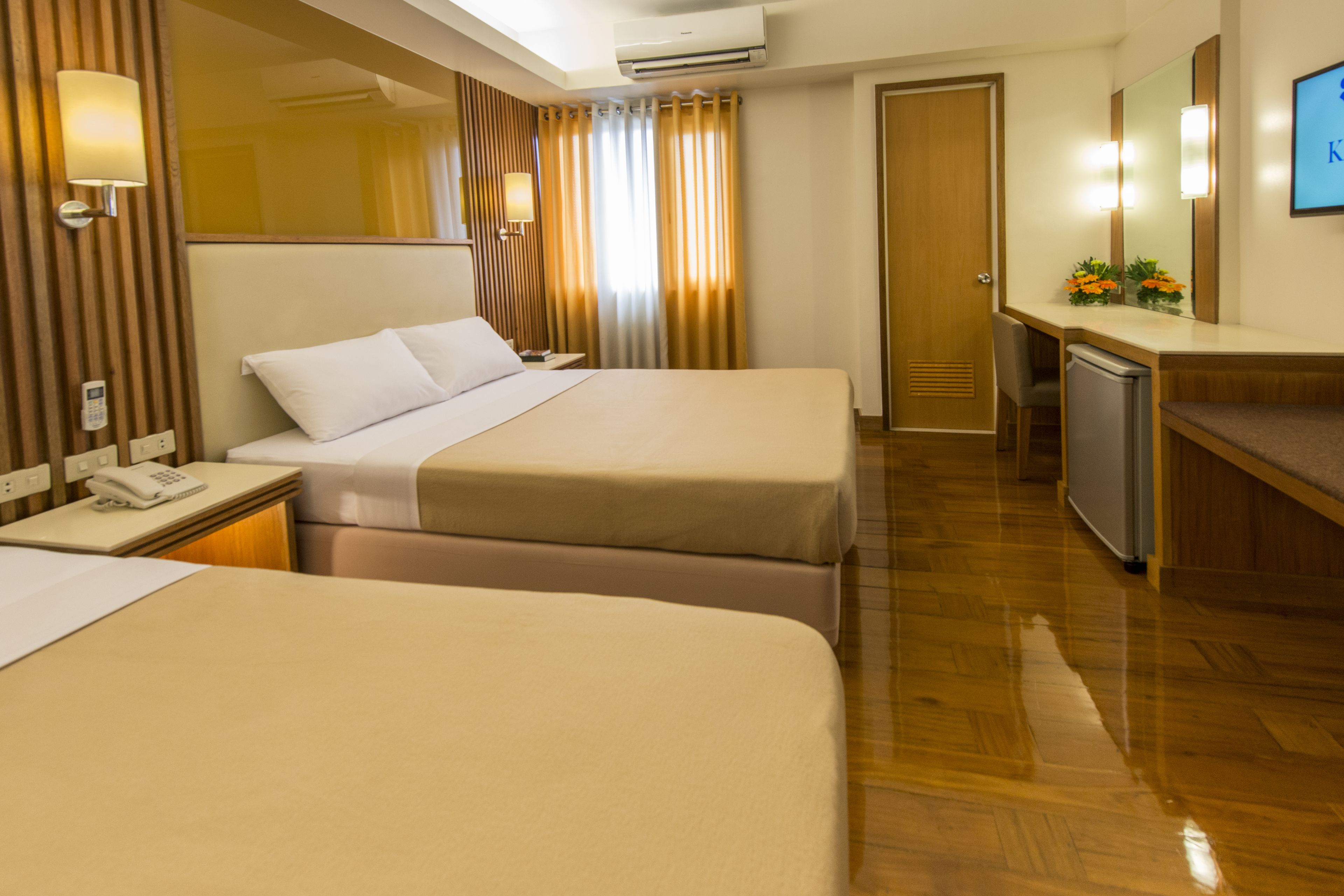 A hotel room with two beds, a desk with a computer, a phone, and a mirror.