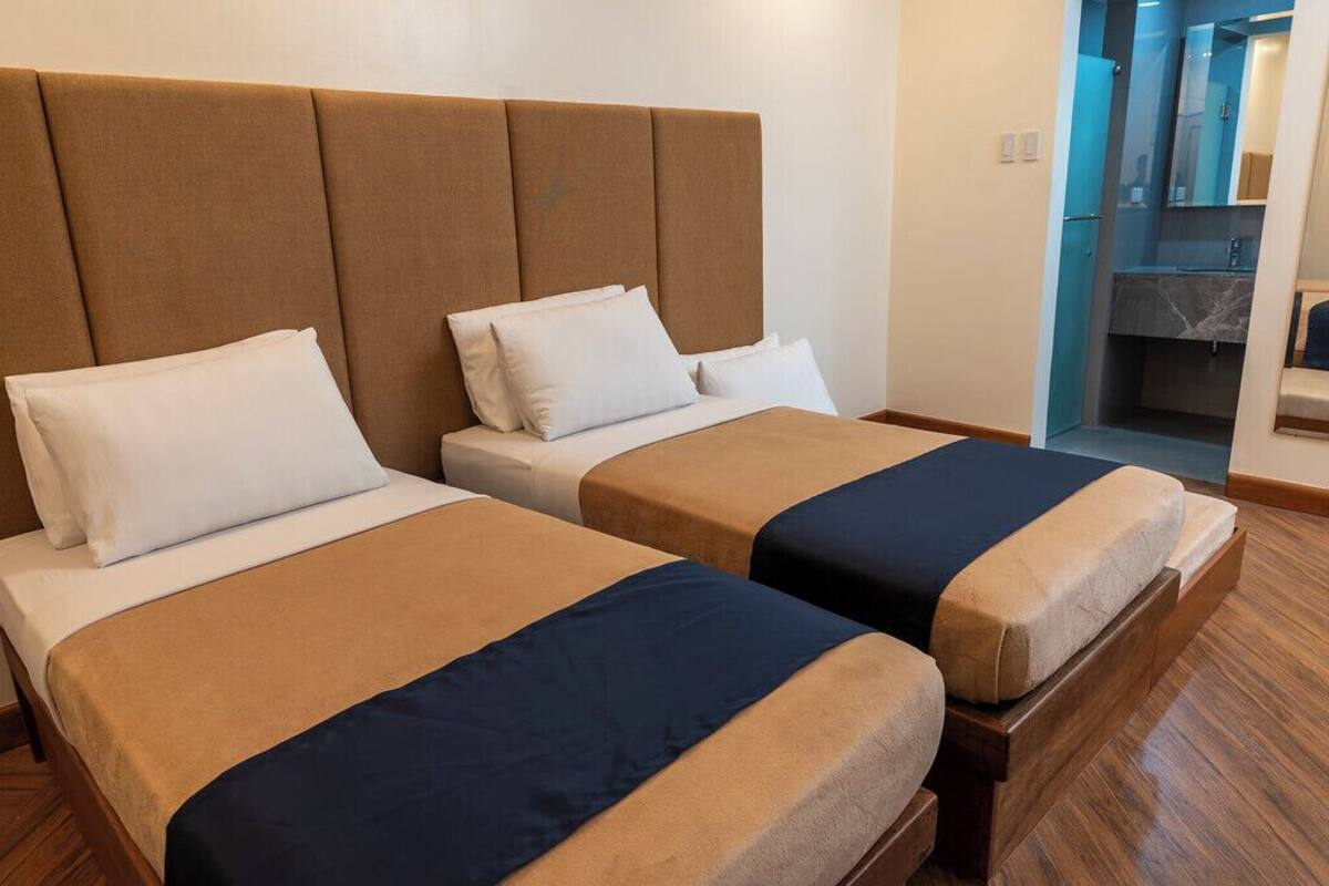 Two beds with headboards, a bathroom with a mirror, and a wooden floor.