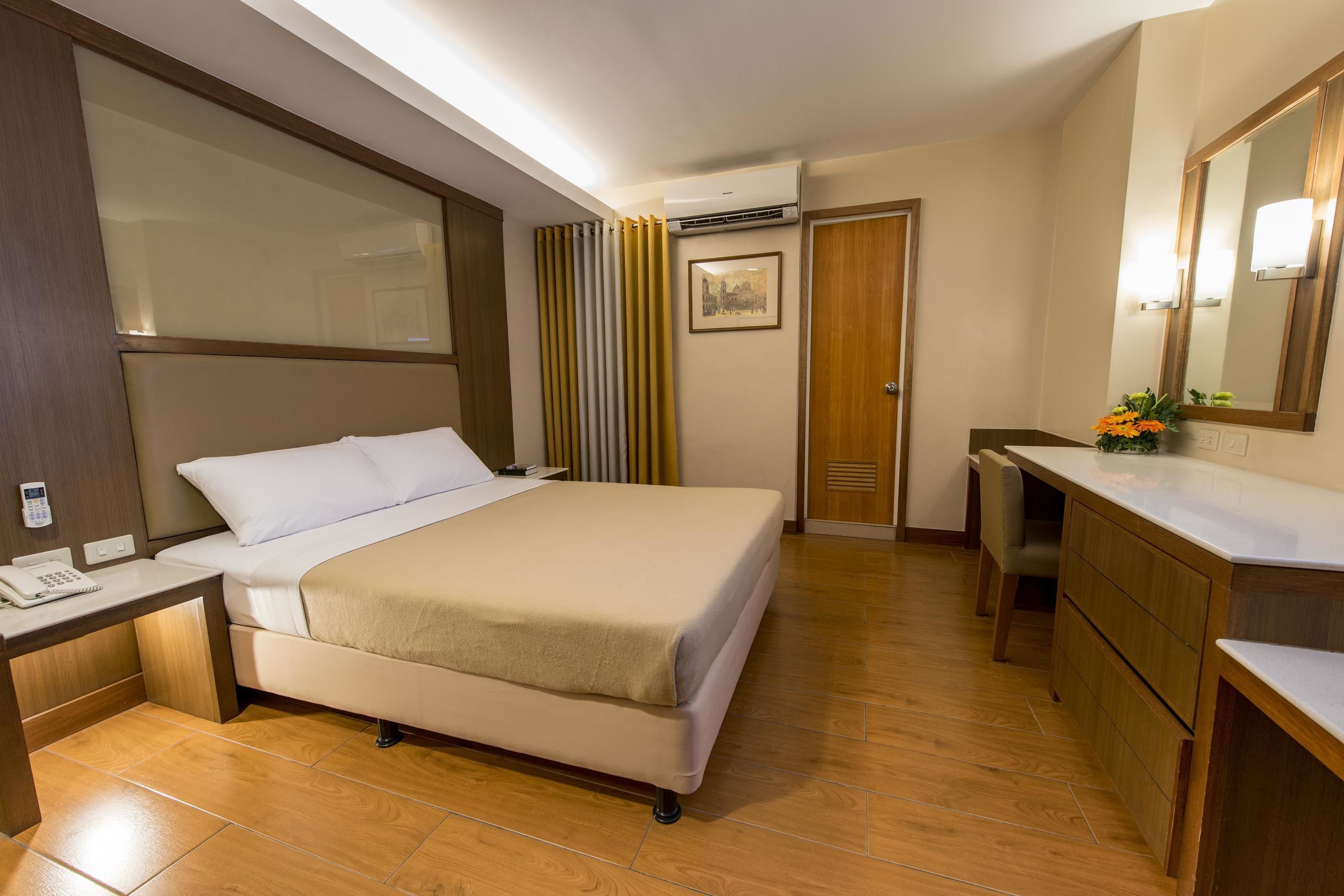 Une chambre d’hôtel équipée d’un lit, d’une table de chevet, d’un miroir et d’un bureau avec un téléphone.