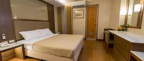 A hotel room with a bed, bedside table, mirror, and a desk with a telephone.