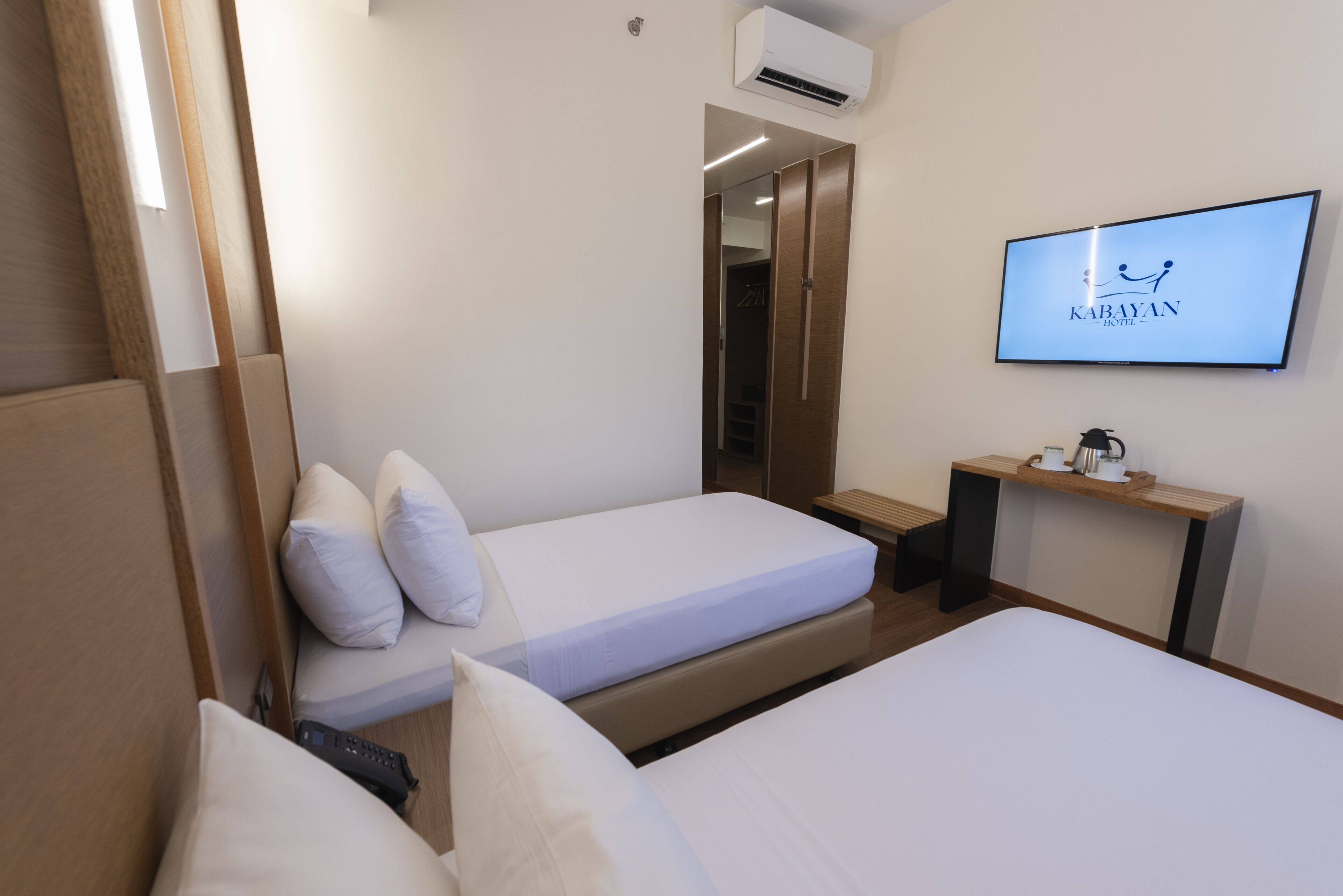 Quarto de hotel com duas camas, televisão, escrivaninha e guarda-roupa.