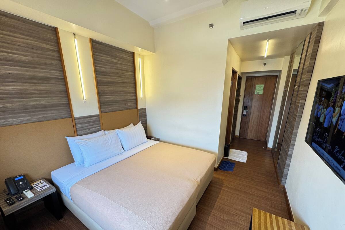 A hotel room with a large bed, bedside table with a phone, and a wall-mounted TV.
