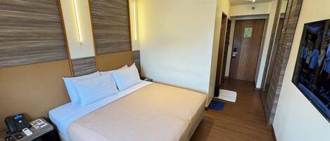 A hotel room with a large bed, bedside table with a phone, and a wall-mounted TV.