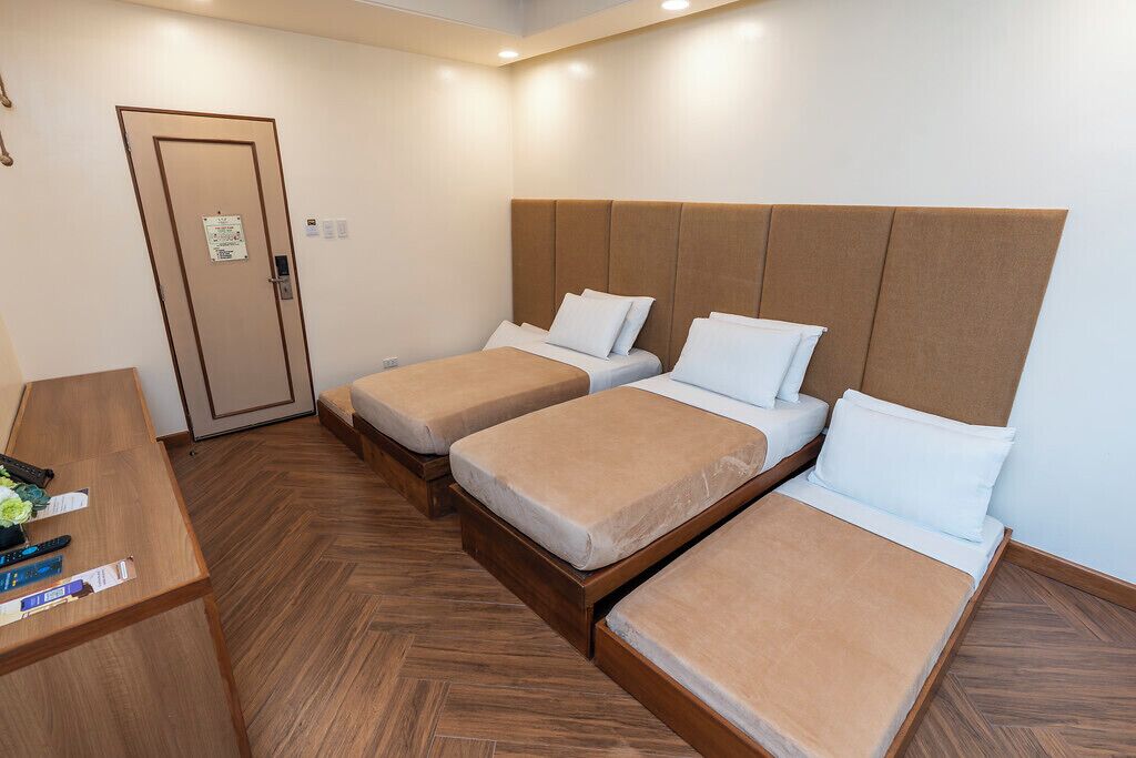 Una habitación de hotel con dos camas individuales, un escritorio de madera y una puerta con un cartel.
