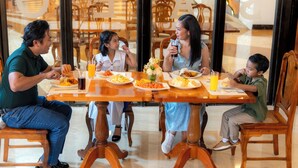 Una família dinueig en un restaurant amb mobiliari de fusta i un separador de vidre.