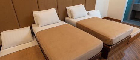 A hotel room with two single beds, a padded headboard, and a wooden floor.