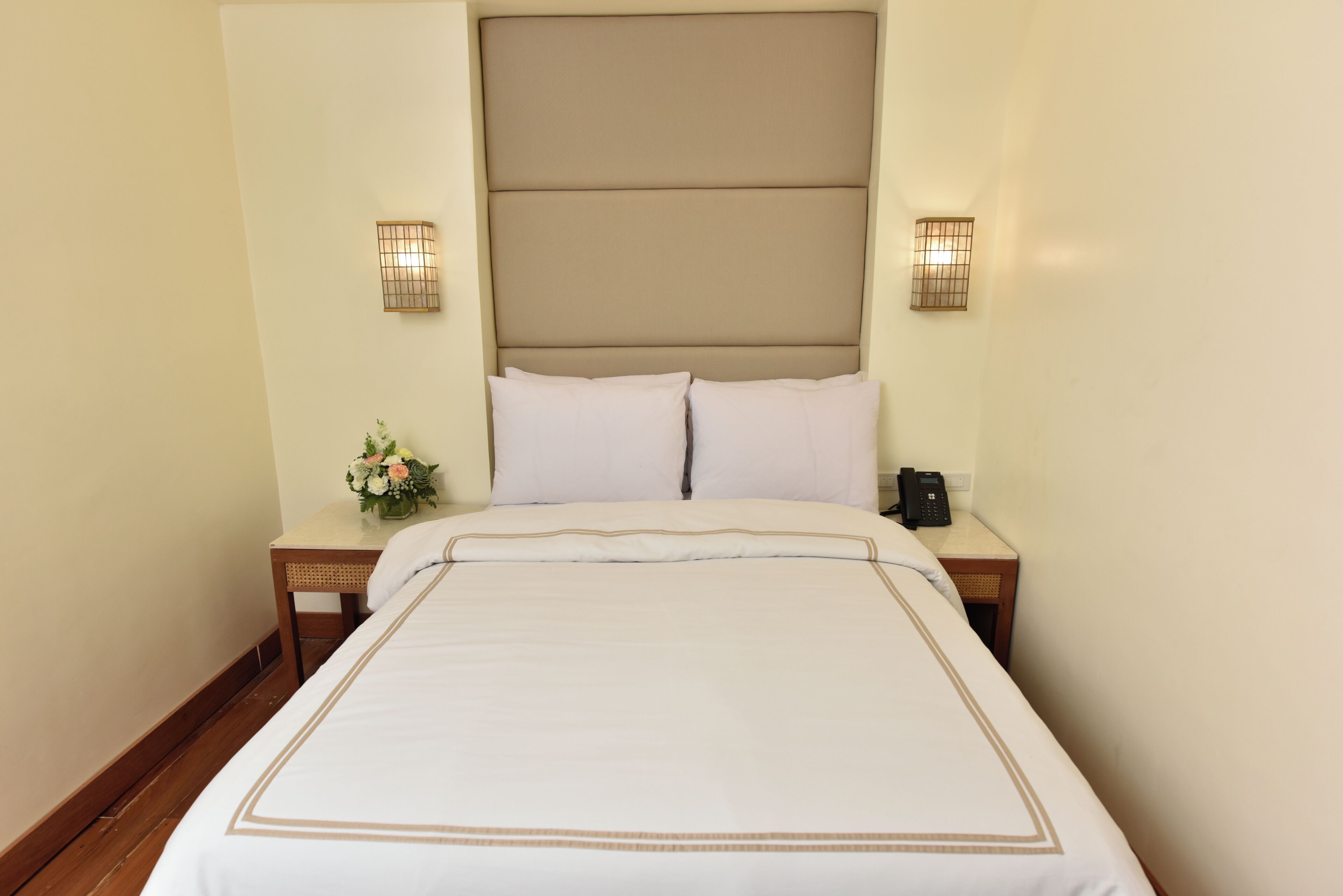 Habitación de hotel con una cama grande, dos mesitas de noche, un teléfono en la pared y dos apliques.