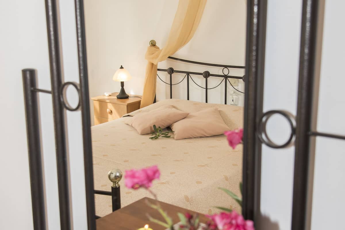 A bedroom with a bed, nightstand, lamp, and a vase with flowers.