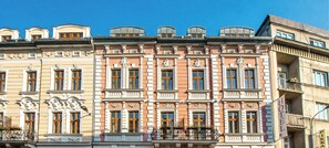 Une rangée d’immeubles à étages, dotés d’éléments architecturaux classiques, notamment des encadrements de fenêtres ouvragés et des éléments décoratifs.