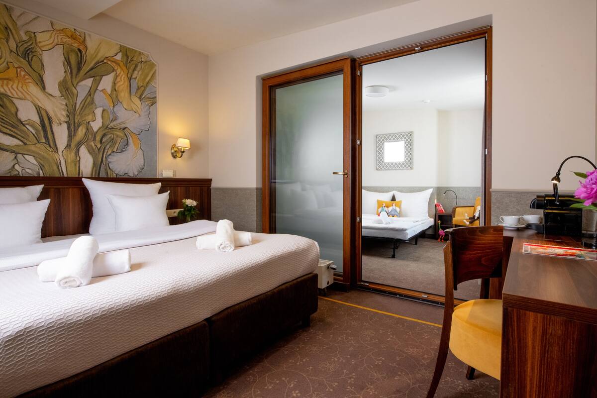 A hotel room with a large bed, a wooden desk, and a sliding glass door leading to a balcony.