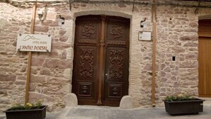 A stone building with a large wooden double door, a sign reading "HOTEL DU CHATEAU L'ANTIC PORTAL", and two flower planters on the ground. - Hotel L'Antic Portal (Vilafames)