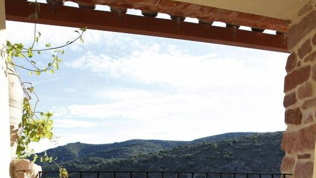 A balcony with a table and chairs, offering a view of a hillside town. - Hotel L'Antic Portal (Vilafames)