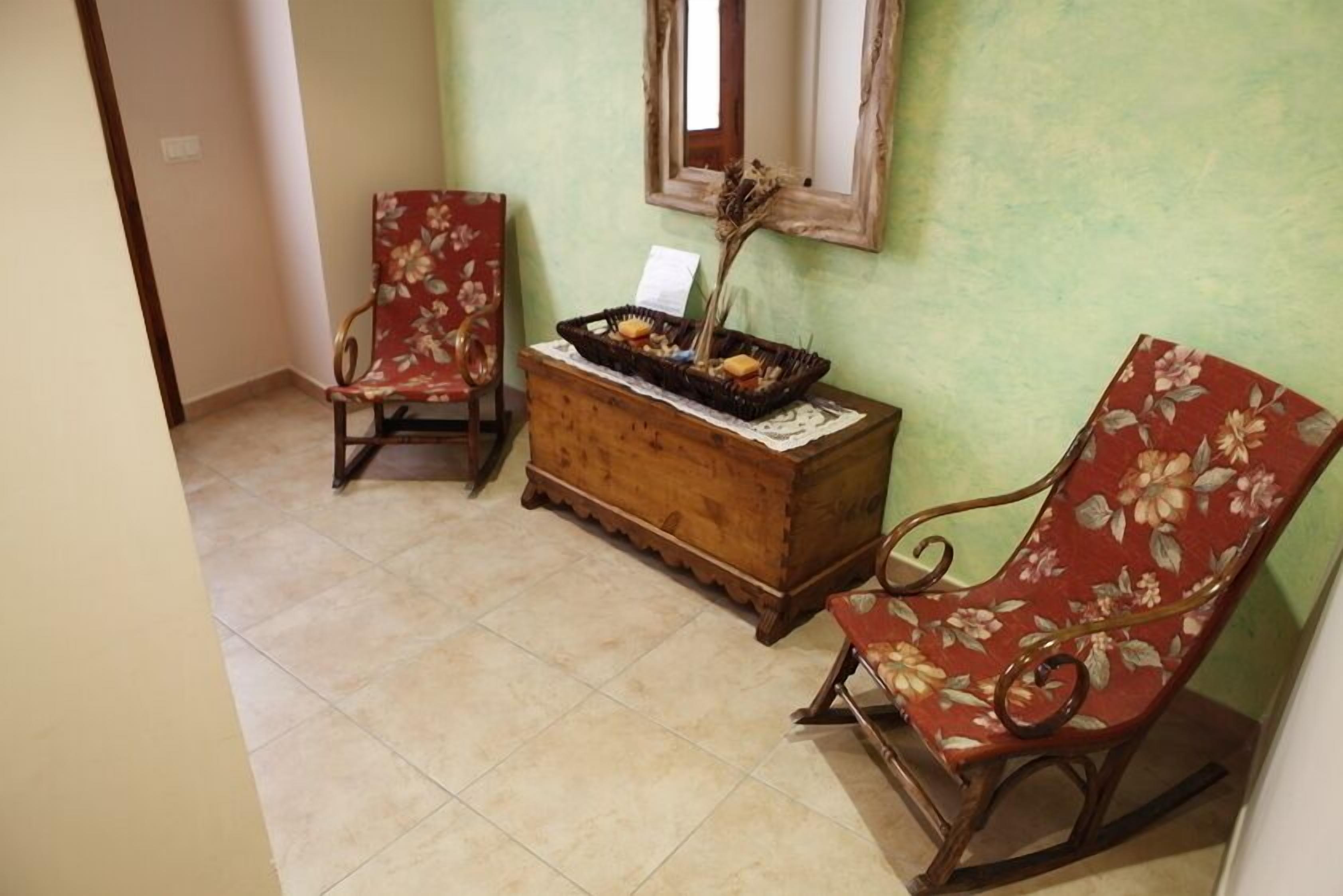 A room with two wooden rocking chairs with floral upholstery, a wooden chest of drawers, and a mirror on the wall.