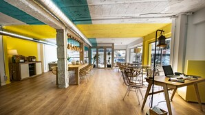 Um escritório amplo com piso de madeira, uma mesa central com cadeiras e uma grande janela com vista para a cidade.
