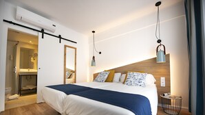 Quarto de hotel moderno com uma cama grande, cabeceira de madeira, mesa de cabeceira com abajur e unidade de ar condicionado.