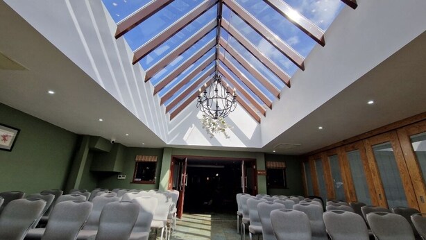 A conference room with a high ceiling and skylight, rows of chairs, and a chandelier. - The Red Lion (Cambridge)