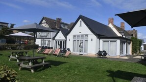 A courtyard with picnic tables and lounge chairs, a white building with large windows, and a traditional black and white house in the background. - The Red Lion (Cambridge)