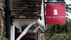A red sign with a lion logo and the text "THE RED LION WHITTLESFORD BRIDGE". - The Red Lion (Cambridge)