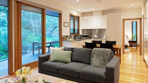 Ein modernes Wohnzimmer mit grauem Sofa, einem Essbereich mit Holztisch und einer Küche mit weißen Schränken.