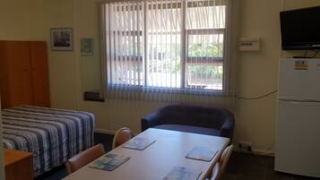 A small room with a bed, a table with chairs, a refrigerator, and a television on a stand.