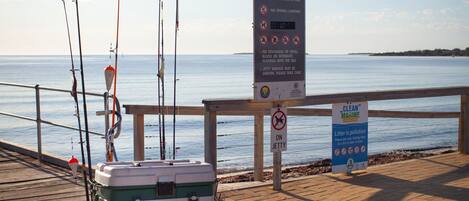 A wooden pier with fishing rods and a cooler, a sign welcoming to Tumbly Bay Jetty, and a 'Clean Marine' pollution awareness sign.