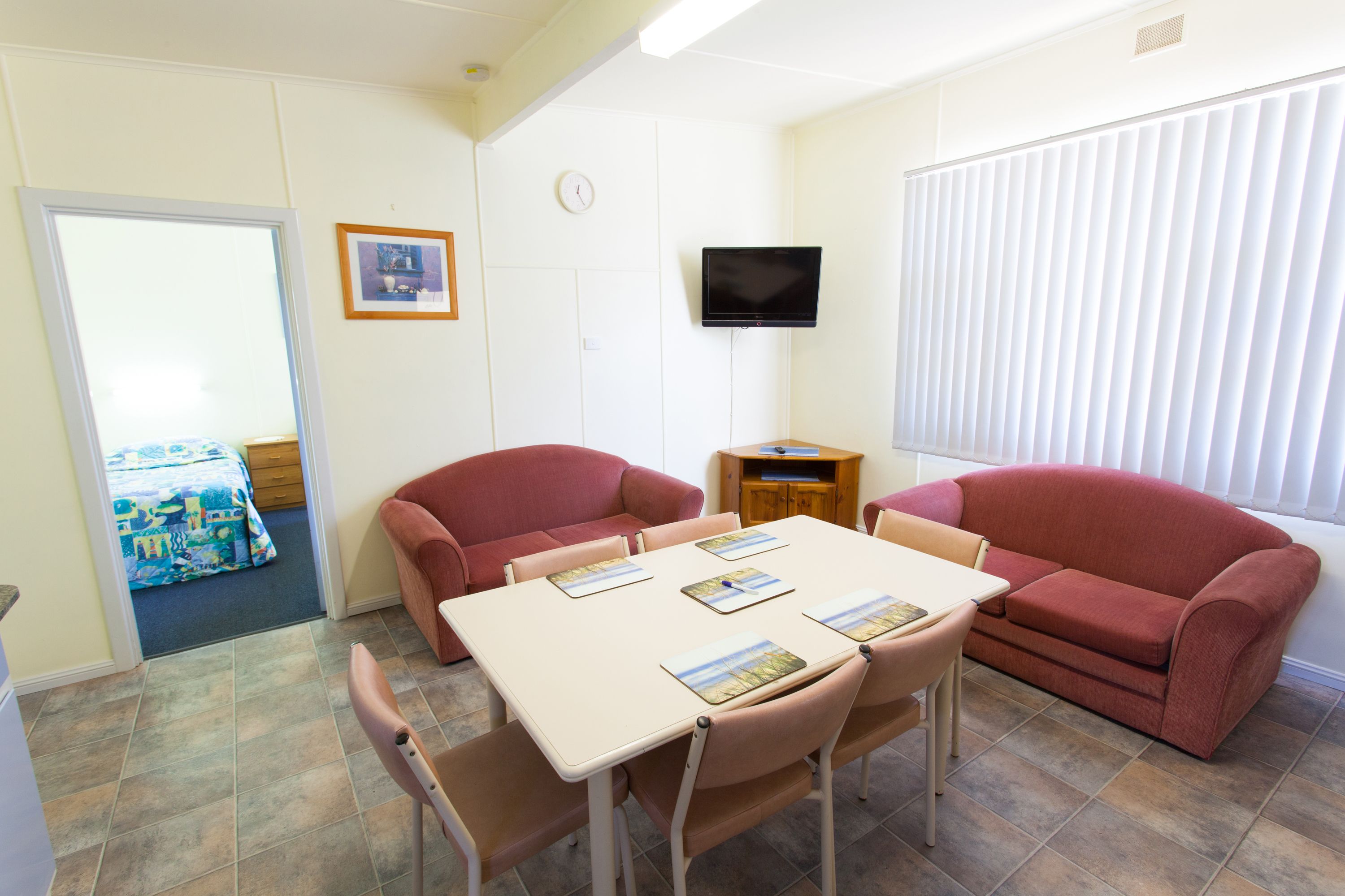 Una habitación con una mesa, sillas, televisor y una ventana con persianas.