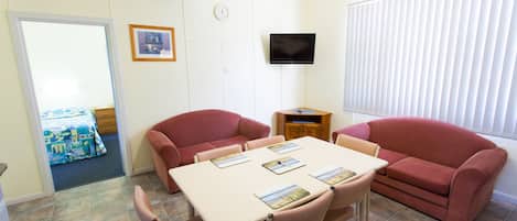 Una habitación con una mesa, sillas, televisor y una ventana con persianas.