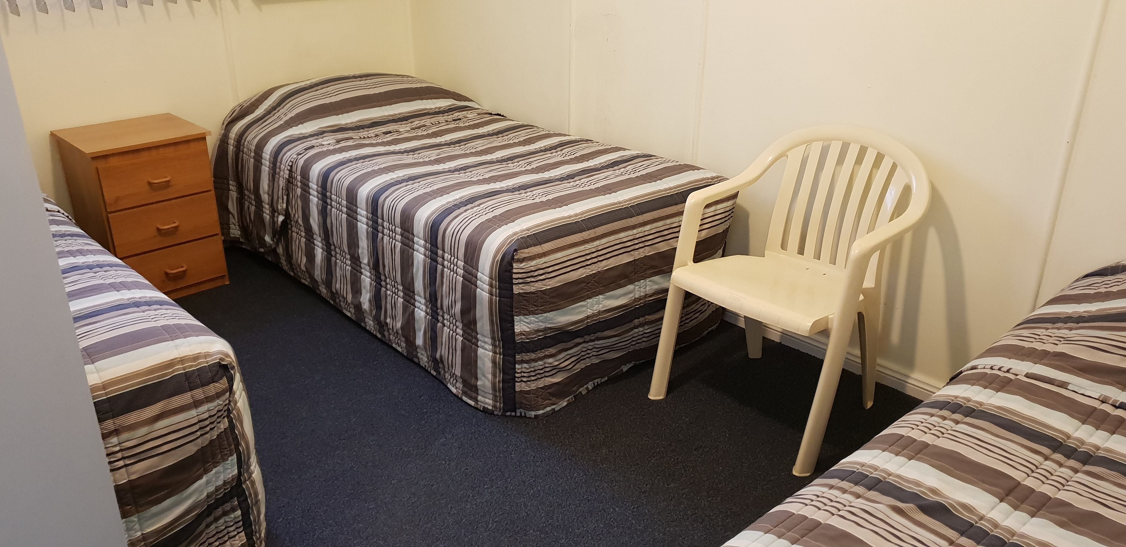 A small, single-room accommodation with a bed, a chair, and a wooden dresser.