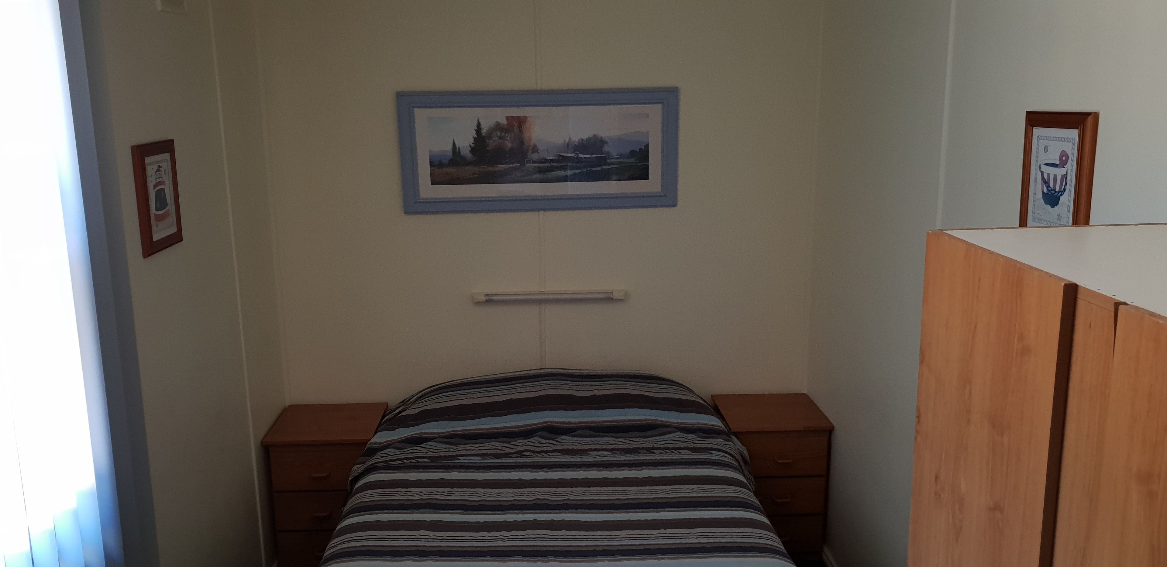 Een slaapkamer met een bed, een nachtkastje, een dressoir en twee foto's in lijsten aan de muur.
