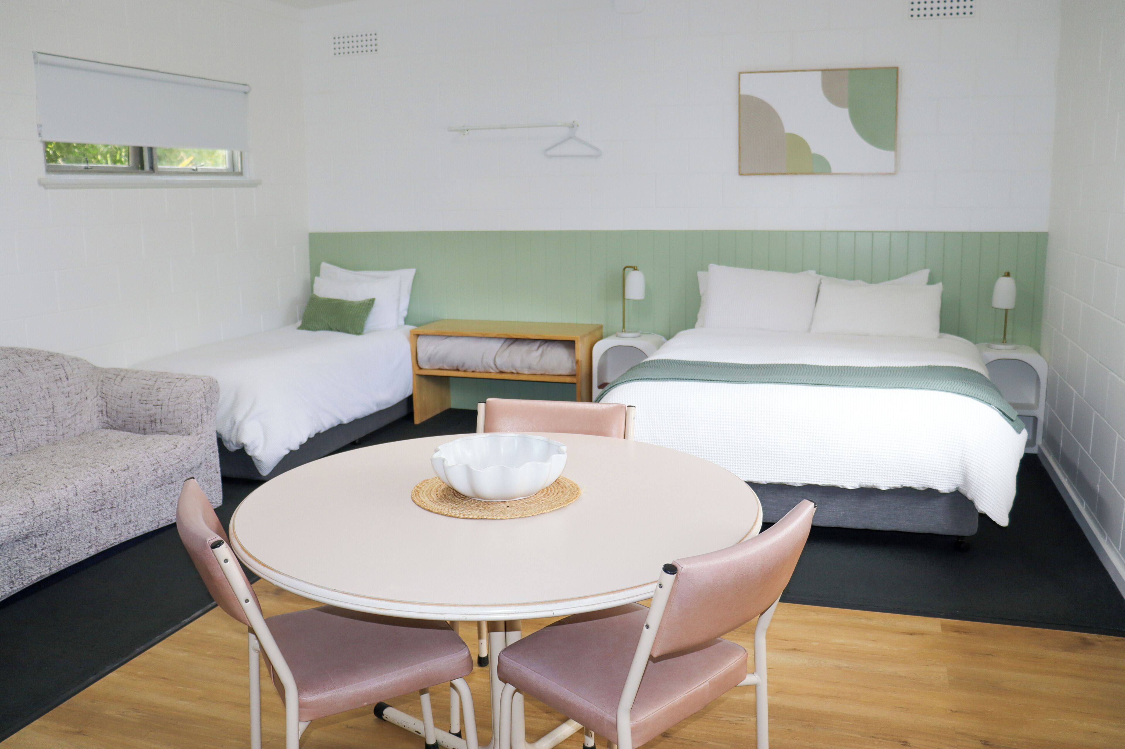 A hotel room with a round dining table, two single beds, a sofa, and a small wooden side table.